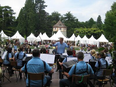 Orchester aus Bühnenperspektive mit Publikum und Schloßpark im Hintergrund